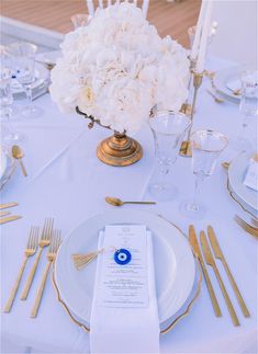 the table is set with white flowers and gold place settings