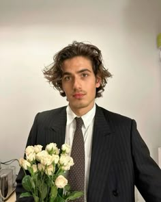 a man wearing a suit and tie holding a bouquet of flowers in front of him