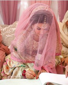 a woman in a veil writing on a piece of paper while another woman looks on