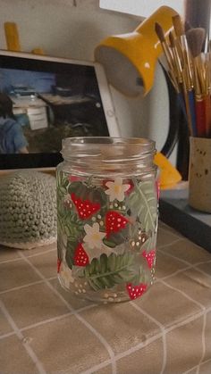 a glass jar sitting on top of a counter filled with pens and pencils next to a computer monitor