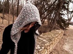 a woman wearing a knitted hat and black jacket is standing by a stone wall