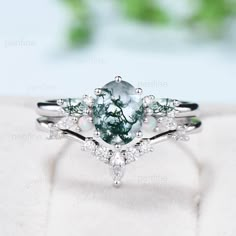 a ring with an oval cut diamond and pear shaped green tourmaline surrounded by white diamonds