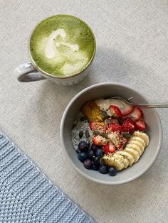 a bowl of fruit and yogurt next to a cup of green tea on a table