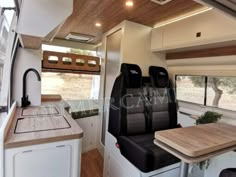 the interior of a camper with wood flooring and white walls, including black seats