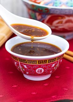 a spoon pouring soup into a bowl with chopsticks on the table next to it