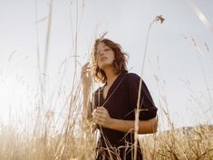 a woman standing in tall grass with her eyes closed