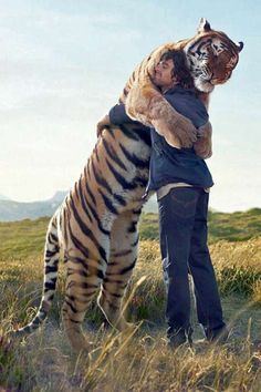 a woman hugging a large tiger on top of a grass covered field