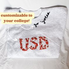 Hand Embroidered Floral College Abbreviation Sweatshirt with Neckline Quote A hand-embroidered crewneck sweatshirt custom to the college of your choice! Cozy up in your college colors and have the coolest gear on campus. Perfect to crop and wear at tailgates! Each sweatshirt is hand embroidered in South Dakota custom to the city of your choice! I use Hanes Men's EcoSmart Sweatshirts and Gildan Adult Fleece Crewneck Sweatshirts, which are both 50% cotton and 50% polyester blends. If there is a di College Colors, Cool Gear, South Dakota, Clothing Items, Hand Embroidered, Crewneck Sweatshirt, Gender Neutral