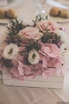 a white box filled with pink flowers and greenery on top of a dining table