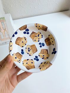 a hand is holding a small bowl with cookies on it and blue dots around the edges