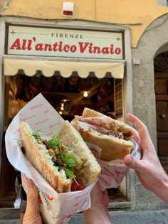 two people holding sandwiches in front of a restaurant