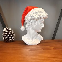 a white busturine wearing a santa hat next to a pine cone on a wooden table