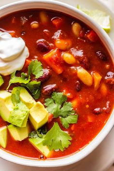 a white bowl filled with chili, avocado and sour cream