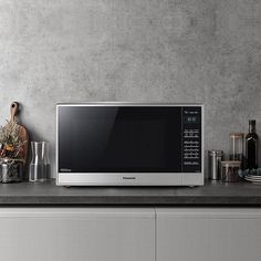 a silver microwave oven sitting on top of a counter next to cups and bowls with utensils