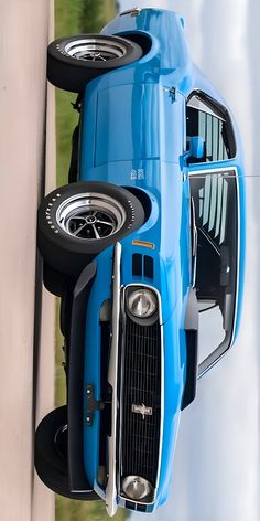 an old blue car hanging upside down on the side of a building with it's hood up