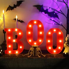 a lighted boo sign sitting on top of a wooden table next to candles and decorations