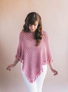 a woman standing in front of a wall wearing a pink crocheted ponchle