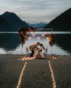 a man and woman kissing in front of some candles on the beach with mountains in the background