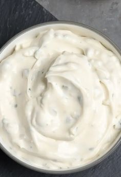 a bowl filled with white cream sitting on top of a black table next to a knife