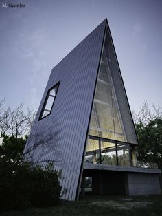 a triangular shaped building with glass windows on the top and bottom floor, in front of trees