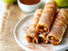 two crepes on a plate with powdered sugar and apples in the background