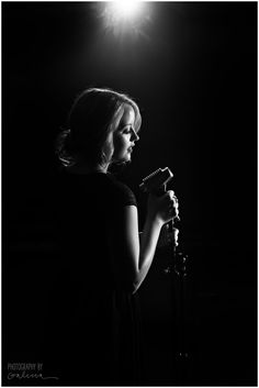 black and white photograph of a woman holding a microphone in front of a bright light