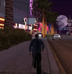 the man is walking down the street in front of some palm trees and buildings at night