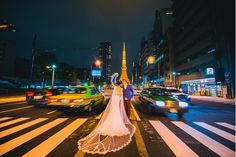 a bride and groom standing in the middle of a crosswalk at night with cars passing by