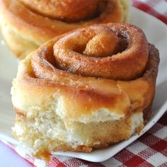 two cinnamon rolls on a white plate sitting on a red and white checkered tablecloth