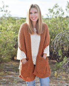 a woman standing in front of some bushes wearing an orange knitted cardigan