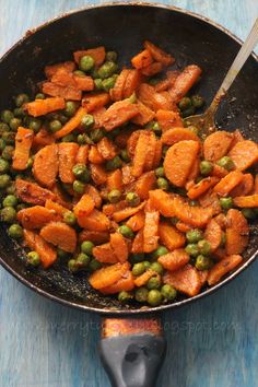 peas and carrots cooking in a skillet on a blue wooden table with a spoon