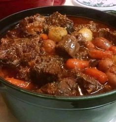 a pot filled with meat and carrots on top of a table next to a plate