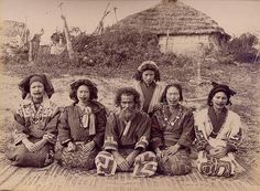 an old black and white photo of people sitting on the ground in front of a hut