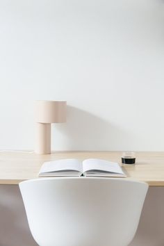 an open book sitting on top of a white chair next to a desk with a lamp