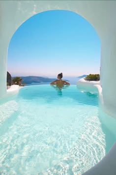 a person sitting in the middle of a swimming pool with clear blue water and white walls