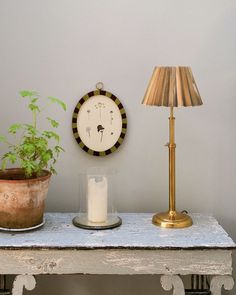 a table with a lamp, clock and potted plant on it