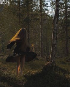 a woman with long blonde hair walking through the woods