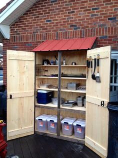 an outdoor storage area with two open doors and several buckets on the floor next to it