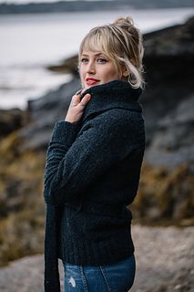 a woman is standing on the rocks by the water with her hand under her chin