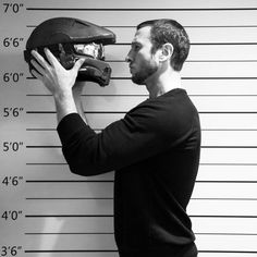 a man in a black shirt is holding a motorcycle helmet and looking at the wall