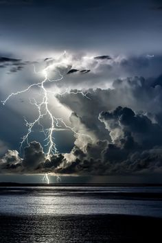 a black and white photo of lightning striking over the ocean with dark clouds in the background