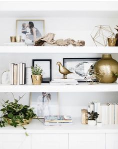 white shelves with gold vases, books and pictures on them in a living room