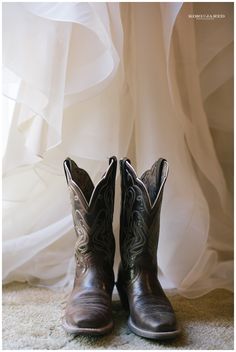 a pair of cowboy boots sitting on top of a carpeted floor next to a white curtain