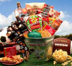 a football and snacks gift basket in a bucket on the grass next to a bowl of popcorn