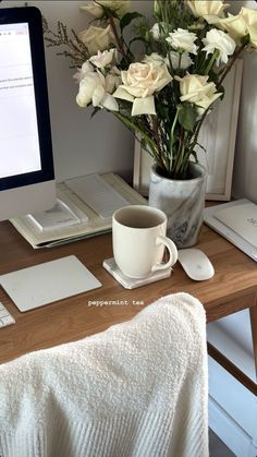 a desk with a coffee cup, laptop and flowers in a vase on top of it