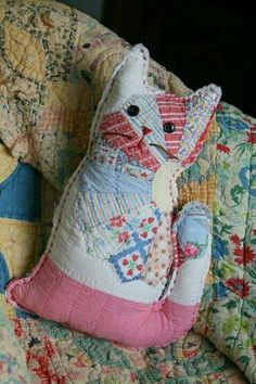 a cat stuffed animal sitting on top of a quilted couch cushion with colorful flowers