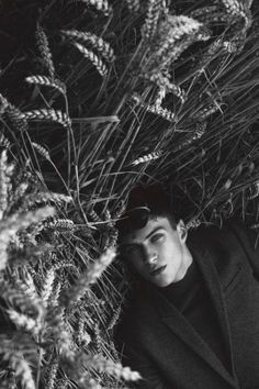 black and white photograph of a man in a coat leaning against a bush with his eyes closed