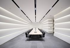 an empty conference room with long tables and chairs in the center is lit by recessed lighting