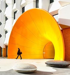 a person walking past a large yellow object in front of a building with white walls