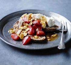 a black plate topped with toast and strawberries next to a fork on top of a table